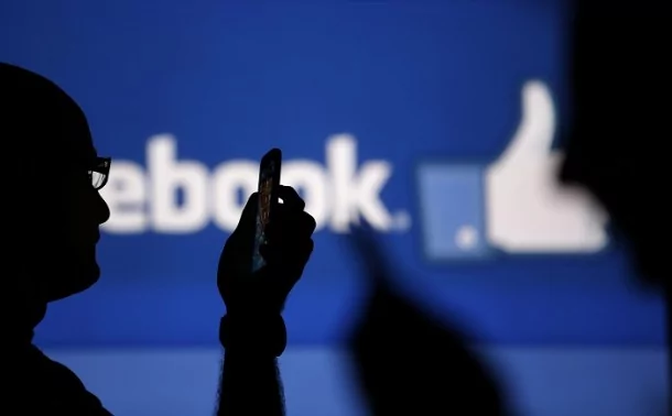 Men are silhouetted against a video screen with an Facebook logo as he poses with an Nokia Lumia 820 and Samsung Galaxy S4 in this photo illustration taken in the central Bosnian town of Zenica